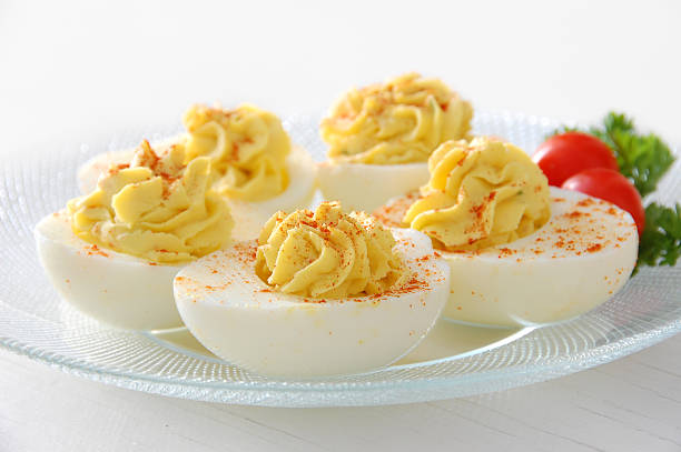 Deviled eggs served on clear plate with grape tomatoes stock photo