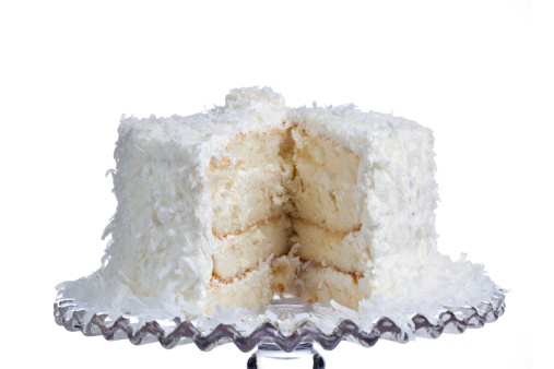 A big slice of cake removed form this coconut cake on a white background sitting on a cake plate.