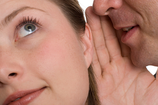 Close-up of young man telling pretty young woman a secret.