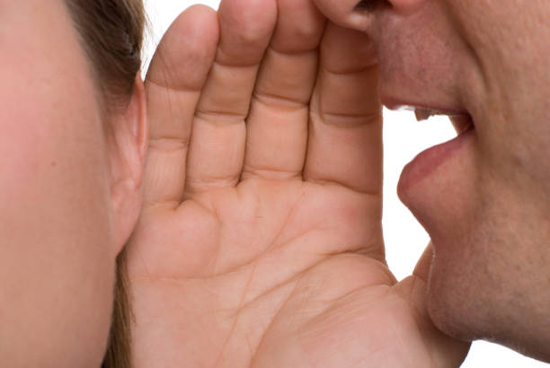 istock Man cupping his hand over a woman's ear telling a secret 182175365