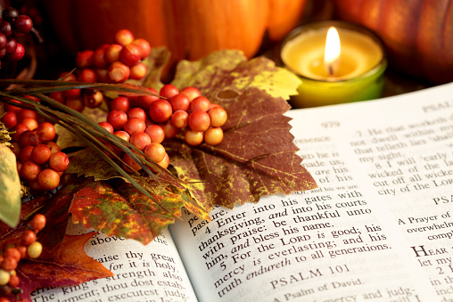Bible is open to Thanksgiving Scripture of Psalms 100:4 with autumn colored leaves, berries, pumpkins and candle. Focus on verse 4. Horizontal image could be used for Christian or religious purposes.