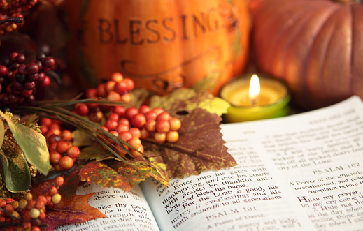 Open Bible showing Scripture Psalms 100:4 with autumn colored berries, leaves and candle. There are two pumpkins in background, one pumpkin is inscribed with \