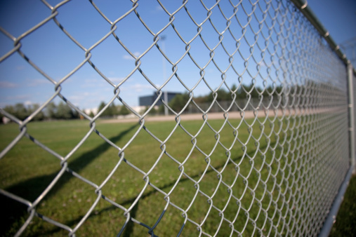 A picture of a chainlink fence on the side of a baseball field.  Selective focus on the fence.