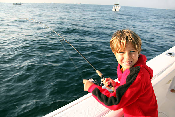 A boy child fishes with his rod against a seascape background on a surf fishing trip in summer.