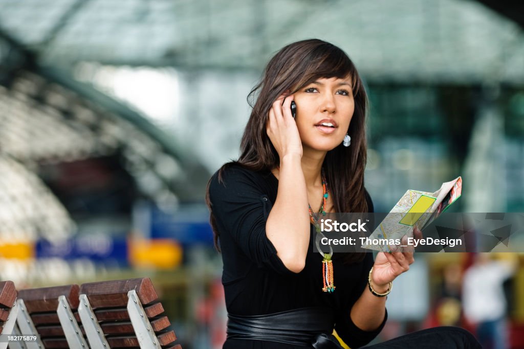 Un giovane brunette donna sul cellulare con una mappa - Foto stock royalty-free di Abbigliamento
