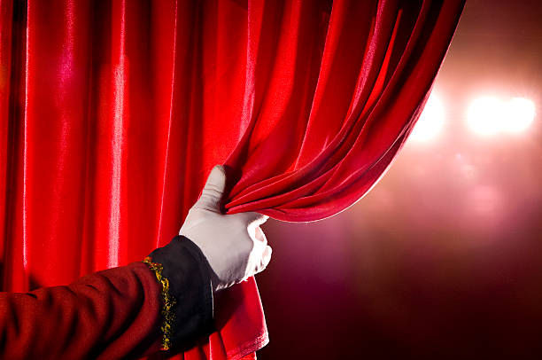 Usher opening red theater curtain, with spotlights "usher, opens red theater curtiain revealing stage lighting...some visible noise in background." performing arts event stock pictures, royalty-free photos & images