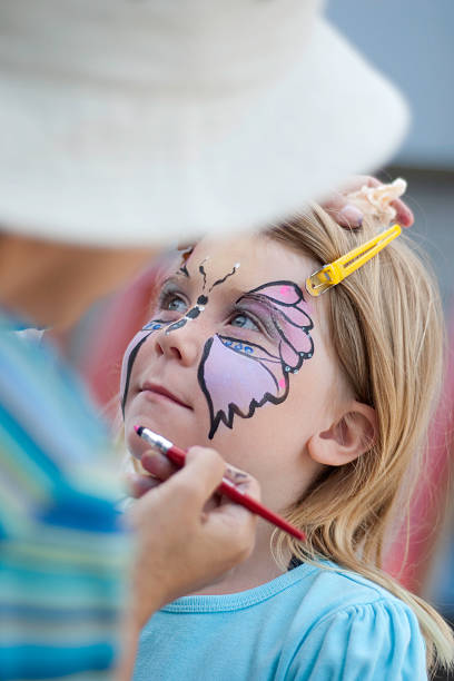 Blond girl getting a butterfly painted on her face A girl getting her face painted. face paint stock pictures, royalty-free photos & images