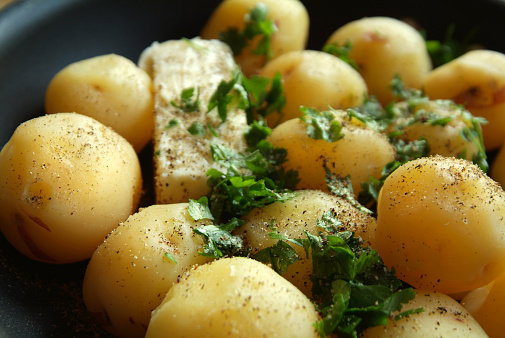 Detail image of peeled new potatoes in a skillet. Fresh butter, parsley, salt and pepper cover the potatoes. Very shallow depth of field, the center of the image is in sharp focus but begins to fade.