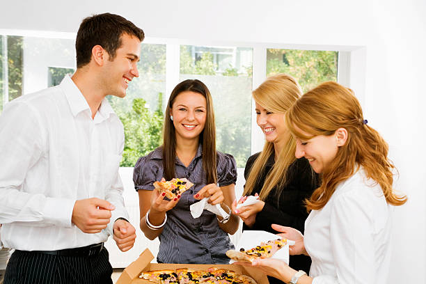 Young coworkers sharing a pizza at lunch break stock photo