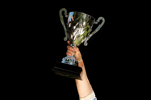 A trophy held aloft in front of black background
