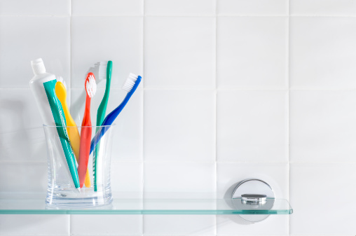 Toothbrushes and fluoride toothpaste on a glass bathroom shelf.