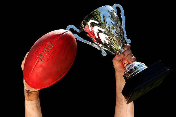 An AFL ball and trophy held aloft in front of a black background