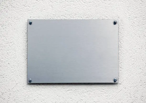 "Blank elegant brushed metal plaque on white wall surface, suitable for logo placement etc."