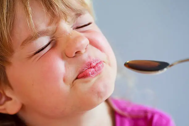 Girl grimaces in front of a spoon of bitter medicine.