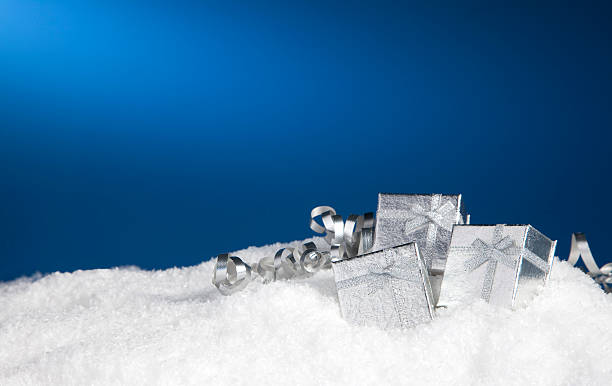 Gift Boxes &lightboxISilver gift boxes nestled in the snow on a blue background. artificial snow stock pictures, royalty-free photos & images