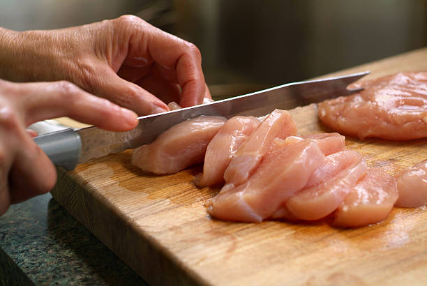Woman Cutting Raw Chicken on a Wooden Cutting Board stock photo
