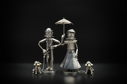 Metal figure of a gentleman and lady with mutual umbrellas walking their 2 dogs