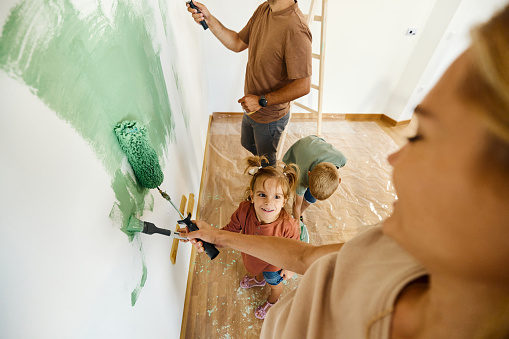 High angle view of happy parents and their small kids cooperating while painting their walls during home renovation process. Copy space.