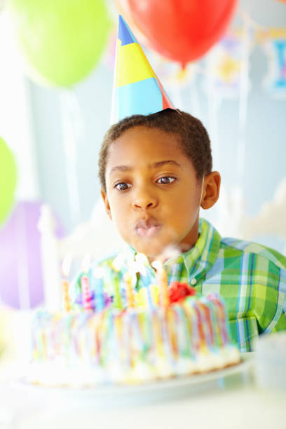Portrait of a little boy in party cap blowing candles on cake