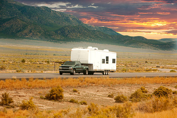 Truck and RV driving down road An RV heads down a scenic road at sunset. towing stock pictures, royalty-free photos & images