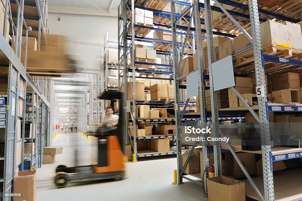 Warehouse Indoor manufacturing and storage details. Warehouse aisle with shelving and a forklifter, cardboard boxes and other merchandise. Blue-collar Worker Stock Photo