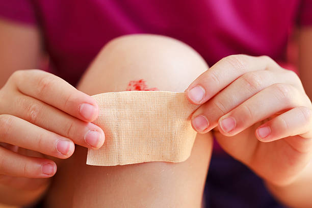 A child putting a plaster on a bloody knee stock photo