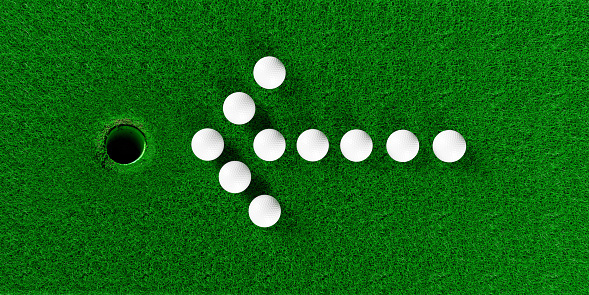 Winning concept. Golf balls arranged in the shape of an arrow pointing to the golf hole. Large copy space on green grass.