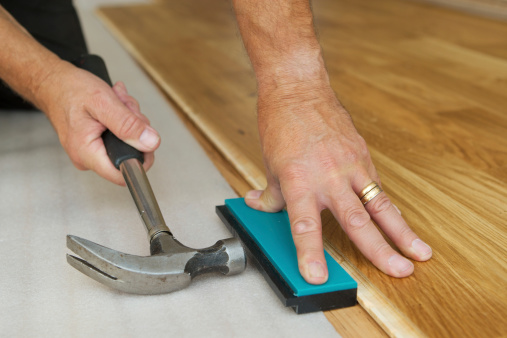 A man installing a wooden floor (oak). Focus is on the left hand.Same series: