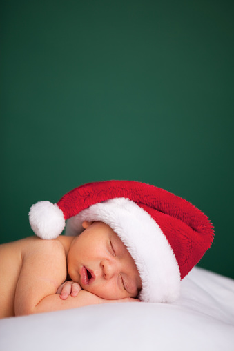Color photo of a newborn baby wearing a Santa hat for Christmas. Room for text above.