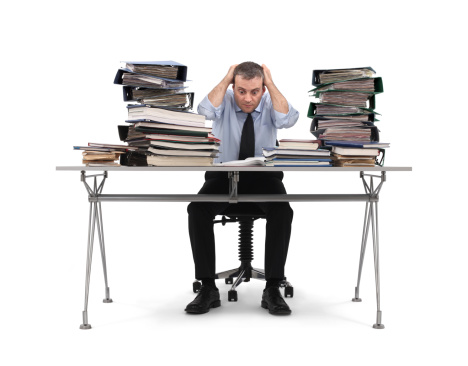 A bored businessman sitting at the office table. Stack of file folders on the table. Isolated on white background.