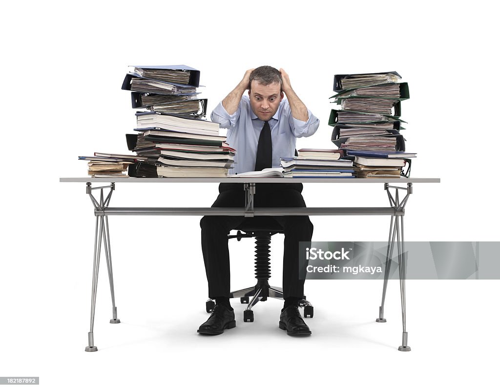 Paperwork A bored businessman sitting at the office table. Stack of file folders on the table. Isolated on white background. Desk Stock Photo