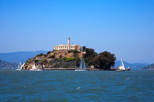 A gorgeous view of the ocean around Alcatraz island Alcatraz island from a small distance with sailboats. alcatraz island photos stock pictures, royalty-free photos & images