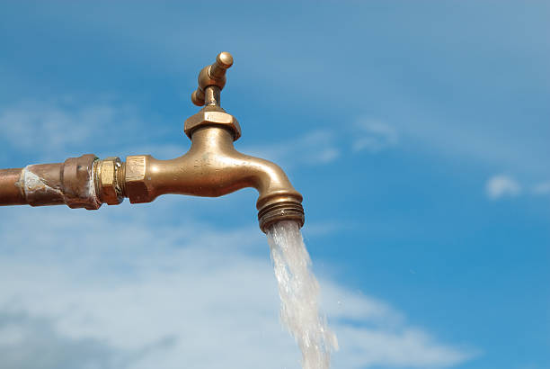 Open water faucet against a blue sky Image of a faucet spouting water. Useful image for any theme involving ecosystems, agriculture, drought, and conservation. faucet stock pictures, royalty-free photos & images