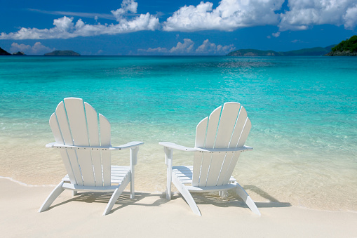 pair of white adirondack chairs on a beautiful beach in the Caribbean