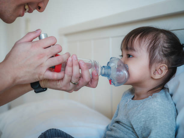 ayah membantu putrinya mendapatkan bantuan dengan spacer inhaler asma saat mengatur di kamar tidur di rumah - sesak napas potret stok, foto, & gambar bebas royalti