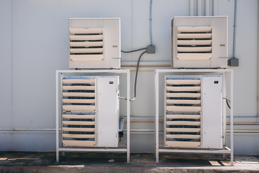 Air conditioner compressor installed on the wall of a building, along with industrial air conditioning units and ventilation systems. Cooling systems.