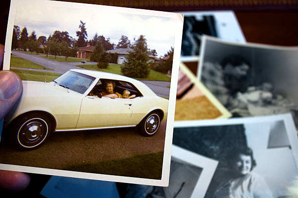 Vintage photograph of mother and child in car Hand holds vintage photograph of mother and child showing off a classic new car with pile of old photos in background. Please view my collectors car photos stock pictures, royalty-free photos & images
