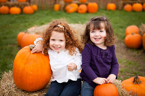 due bambine sorridenti in un campo di zucche - pumpkin child little girls pumpkin patch foto e immagini stock
