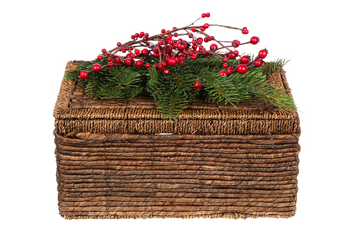 Closed wicker picnic basket decorated for Christmas with pine twigs and holly berries ornaments isolated on white background