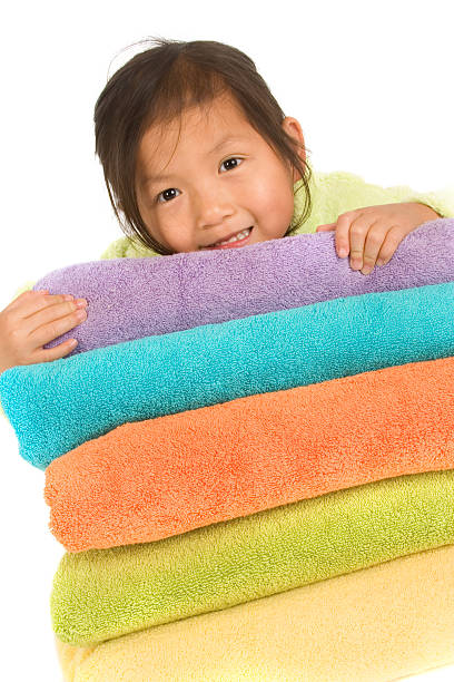 Chinese little girl looking over stack of multi-colored towels