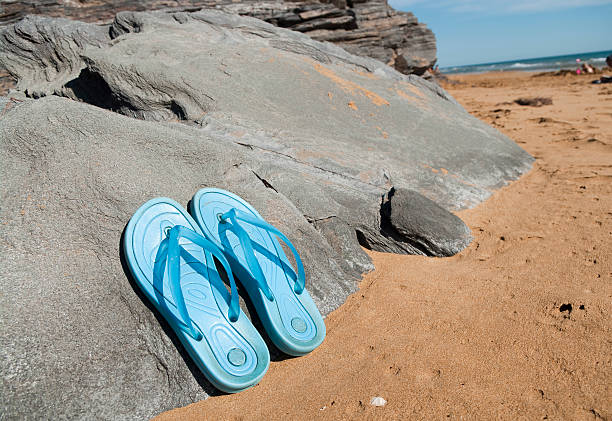Summer slippers on the beach near the water. Sea shells on a sunny day. Tropical beach vacation and travel concept