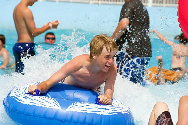 A teenaged boy enjoys riding on an inflatable tube at a water park in the the wave pool.