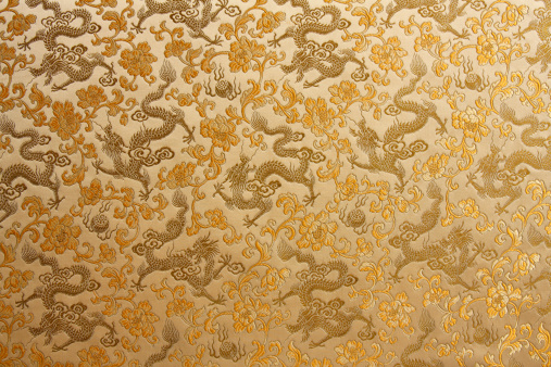 A close-up detail of a Asian gold embroidered fabric with repeated Chinese Dragon and flower design