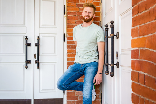 Portrait of Smiling Young Redhead bearded Man with red Facial Hair standing at old Brick Wall.Sunny summer day.