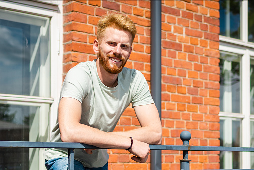 Portrait of Smiling Young Freckled Redhead bearded Man with red Facial Hair standing at old Brick Wall.Sunny summer day.