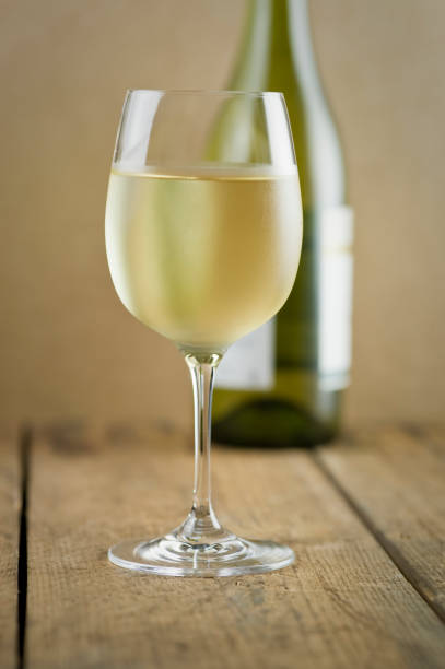 Glass of white wine, bottle and wood table stock photo