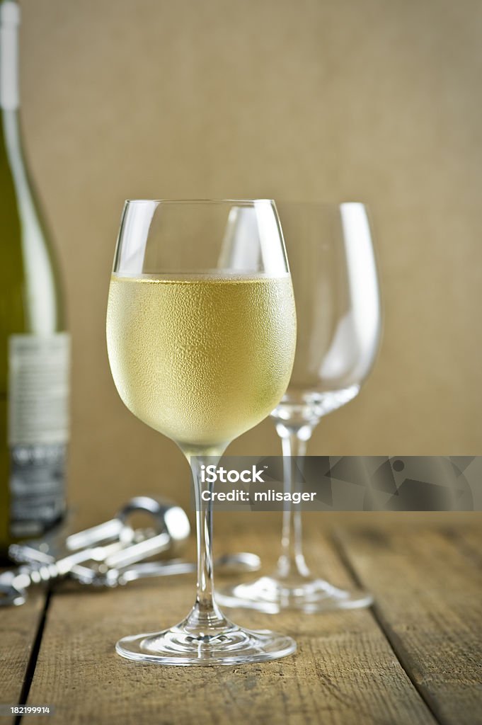 White wine, corkscrew, bottle, table "Wine tasting in a cellar, white wine in a glass to the foreground, empty wine glass, bottle of wine and silver corkscrew opener to the background on a wooden table with clay background." Alcohol - Drink Stock Photo