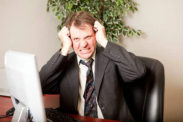 Stressed-out businessman at office desk pulling out hair in frustration.