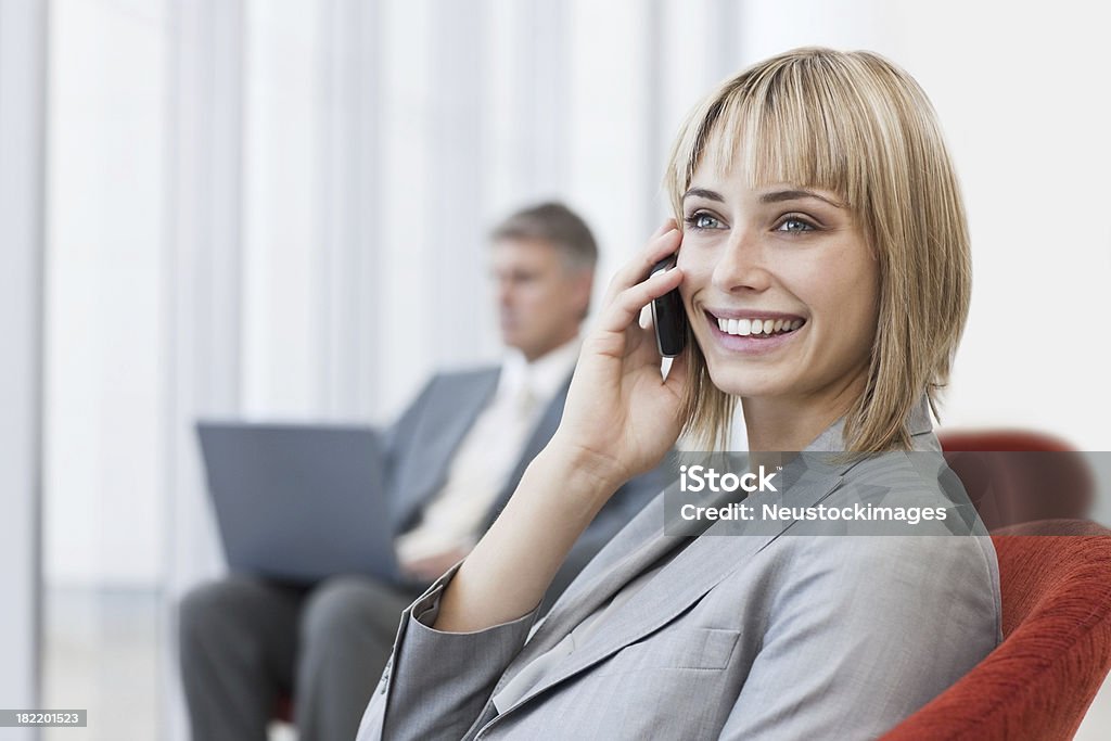 Happy businesswoman using cellphone with colleague in the background Happy young businesswoman using cellphone with colleague in the background 20-24 Years Stock Photo