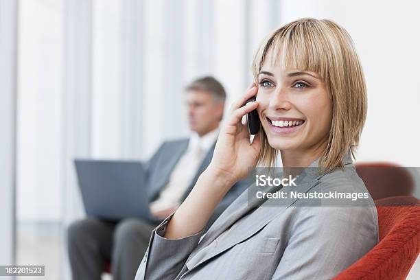 Happy Businesswoman Using Cellphone With Colleague In The Background Stock Photo - Download Image Now